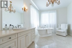 Spa-inspired primary bathroom featuring a freestanding soaking tub, dual-sink vanity with cream cabinetry and polished countertops, large framed mirror, polished stone flooring, ornate brass chandelie - 