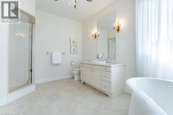 Freestanding bathtub, glass-enclosed shower, single vanity with integrated sink, full-height mirror, and light-toned tile flooring - 