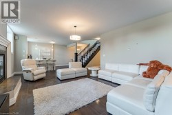 Open-concept living area featuring hardwood flooring throughout, recessed ceiling lighting, a gas fireplace with surround, and a curved staircase with wrought-iron railings - 