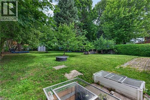 Expansive backyard featuring mature trees, a manicured lawn, a fire pit, a storage shed, and a privacy hedge - 114 Shuh Avenue, Kitchener, ON 