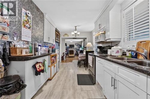 Galley kitchen featuring wood-finish flooring, white cabinetry, dark countertops, and a double basin sink - 121 Panin Road, Burlington, ON 