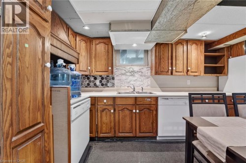 Wood-finish cabinetry with white knobs, dual-basin stainless steel sink, hexagonal tile backsplash, and white countertops - 121 Panin Road, Burlington, ON 