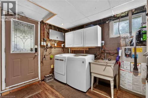 Utility room featuring wood-finish flooring, a decorative glass-paneled door, upper cabinetry, and a utility sink - 121 Panin Road, Burlington, ON 