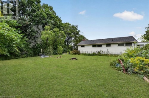 Expansive grass lawn with surrounding mature trees and foliage, featuring a white-sided exterior with multiple windows and a dark shingled roof - 121 Panin Road, Burlington, ON 