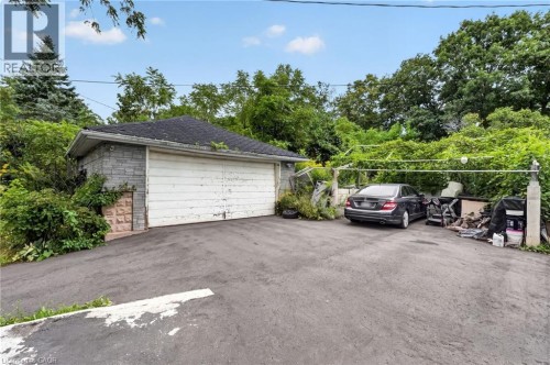 Asphalt driveway with an attached garage featuring a single overhead door and stone-finish exterior - 121 Panin Road, Burlington, ON 