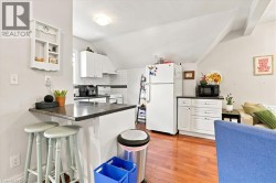 Kitchen area featuring wood-finish flooring, white cabinetry, dark countertops, and a subway tile backsplash - 