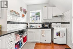 Kitchen featuring hardwood flooring, white subway tile backsplash with accent band, white cabinetry, integrated sink, and built-in appliances - 