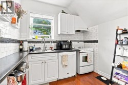Kitchen featuring white subway tile backsplash with a dark accent band, white cabinetry, integrated stainless steel sink, and wood-finish flooring - 