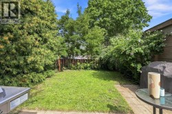 Expansive backyard featuring a lush lawn, mature trees, wood fence, and a paved patio area - 