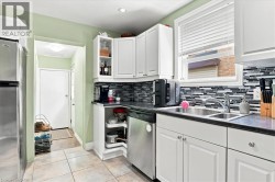 Stainless steel dishwasher, dual basin sink with chrome faucet, black countertops, white cabinetry with silver hardware, and a mosaic tile backsplash - 