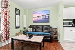 Hardwood flooring, light green wall paint, white cabinetry with silver hardware, black countertop, and recessed lighting - 