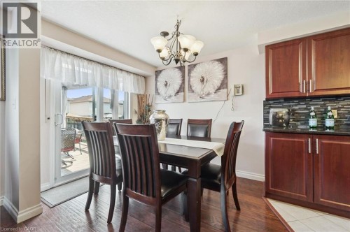 Hardwood-finish flooring, sliding glass door with deck access, built-in cabinetry with dark countertop, tiled backsplash, and an overhead chandelier - 86 Bridlewreath Street, Kitchener, ON 