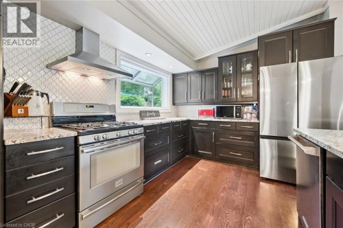 Stainless steel appliances, wood-finish flooring, dark wood cabinetry, light-toned countertops, and a full tile backsplash - 100 Forest Hill Drive, Kitchener, ON 