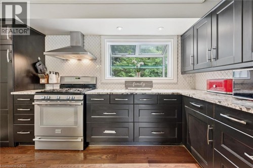 Dark cabinetry with brushed nickel hardware, stainless steel range with overhead vent, patterned tile backsplash, light-colored countertops, and wood-finish flooring - 100 Forest Hill Drive, Kitchener, ON 