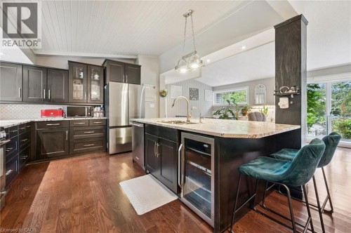Hardwood flooring throughout, a kitchen island with built-in beverage refrigerator, granite countertops, dark wood-finish cabinetry, and stainless steel appliances - 100 Forest Hill Drive, Kitchener, ON 