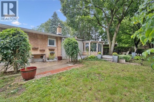 Brick exterior, wood-paneled sunroom, paved patio, mature trees, and a grassy yard - 100 Forest Hill Drive, Kitchener, ON 