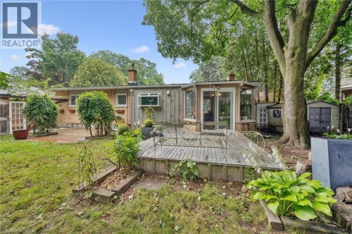 Rear exterior featuring a sunroom, an expansive wooden deck, a brick patio, and mature trees - 100 Forest Hill Drive, Kitchener, ON 