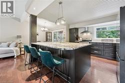 Kitchen featuring a large island with stone countertop, dark wood-finish cabinetry, stainless steel range hood, and wood-finish flooring - 