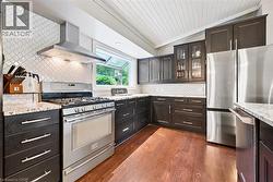 Kitchen featuring stainless steel appliances, dark wood-finish cabinetry, light-toned countertops, a full-height decorative tile backsplash, and wood-finish flooring - 