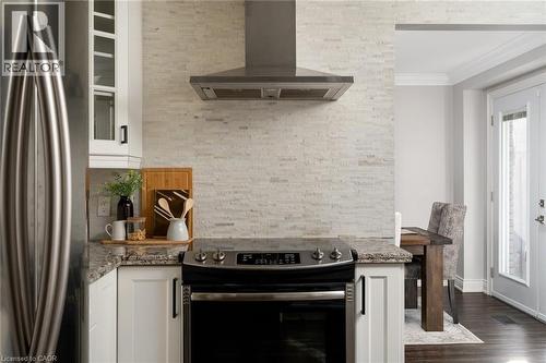 Kitchen featuring a stainless steel range and hood, white shaker-style cabinetry with black hardware, granite countertops, and a full-height stacked stone backsplash - 20 San Marino Crescent, Hamilton, ON 