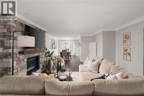 Open-concept living space featuring a stacked stone fireplace with a wood mantel, crown molding, recessed lighting, and wood-finish flooring - 20 San Marino Crescent, Hamilton, ON 