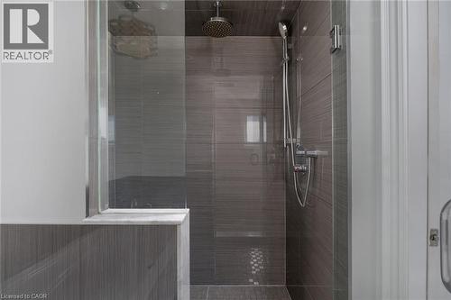 Glass-enclosed shower featuring dark gray tile walls, mosaic tile flooring, a rainfall showerhead, and a handheld shower fixture - 20 San Marino Crescent, Hamilton, ON 
