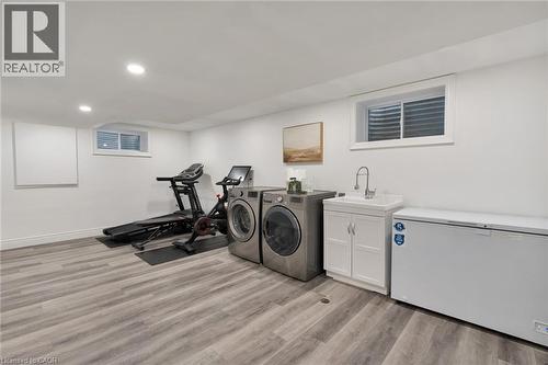 Versatile finished basement space featuring light wood-finish flooring, recessed lighting, and a utility sink with a white cabinet - 20 San Marino Crescent, Hamilton, ON 