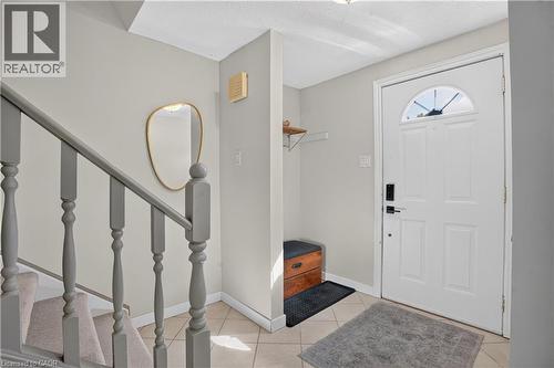 Entryway featuring tile flooring, a white paneled door with an arched transom, and a carpeted staircase with painted balusters - 38 Meadow Woods Crescent, Kitchener, ON 