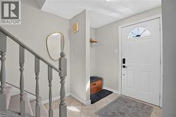 Entryway featuring tile flooring, a white paneled door with an arched transom, and a carpeted staircase with painted balusters - 