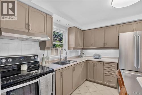 Kitchen featuring beige cabinetry, stainless steel appliances, white tile backsplash, a double basin sink, - 38 Meadow Woods Crescent, Kitchener, ON 
