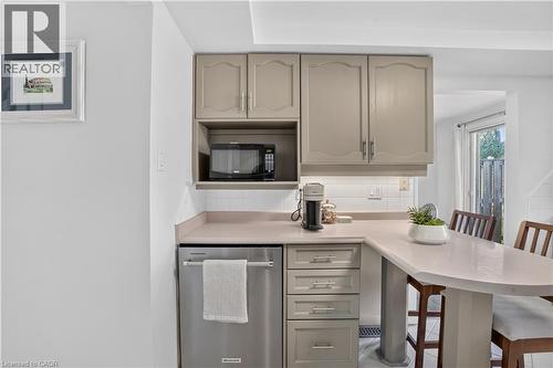 Built-in stainless steel dishwasher, integrated microwave nook, neutral-toned cabinetry, light-toned countertop, and white subway tile backsplash - 38 Meadow Woods Crescent, Kitchener, ON 