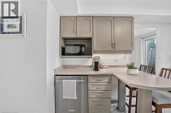 Built-in stainless steel dishwasher, integrated microwave nook, neutral-toned cabinetry, light-toned countertop, and white subway tile backsplash - 