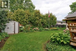Expansive backyard featuring a lush lawn, established garden beds, mature trees, and a functional storage shed - 