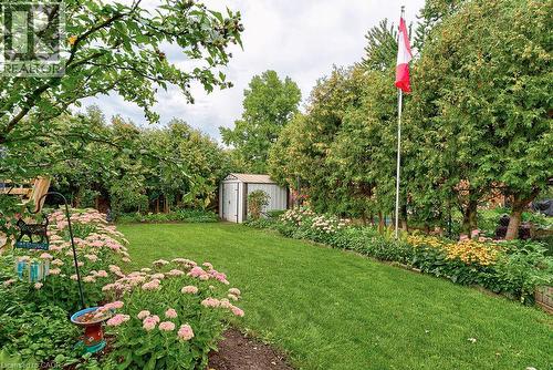 Manicured lawn with mature trees, garden beds featuring various plantings, and a storage shed - 210 Shelley Drive, Kitchener, ON 