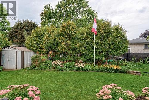 Manicured lawn with a garden bed featuring established plantings and mature trees - 210 Shelley Drive, Kitchener, ON 