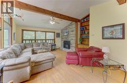 Vaulted ceiling with exposed wood beams, hardwood flooring, stone-clad fireplace, built-in shelving, and large windows - 
