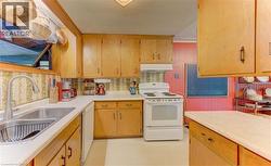 Kitchen featuring light wood cabinetry, white countertops, a double basin stainless steel sink with a high-arc faucet, and a white electric range with an overhead hood - 