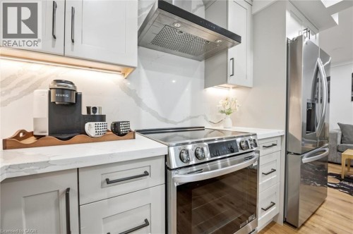 Light-toned cabinetry with dark hardware, quartz countertops, tile backsplash, built-in stainless steel oven with cooktop, and stainless steel refrigerator - 1261 Stephenson Drive, Burlington, ON 