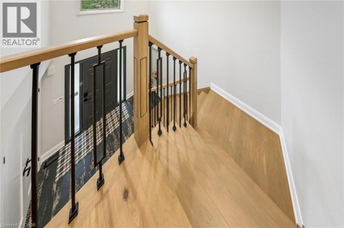 Wood-finish staircase with black metal balusters and a light wood handrail, leading to a dark entry door with frosted glass side panels - 1261 Stephenson Drive, Burlington, ON 