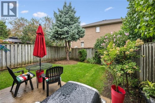 Paved patio area, manicured lawn, perimeter fencing, mature evergreen tree, and brick exterior - 1261 Stephenson Drive, Burlington, ON 