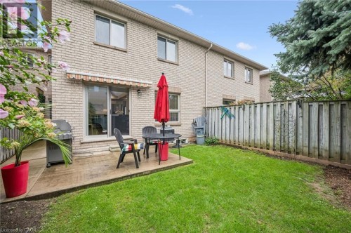 Brick exterior with a ground-level patio, sliding glass door, and a fenced backyard with a grass lawn - 1261 Stephenson Drive, Burlington, ON 