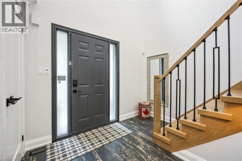 Entryway featuring a dark paneled door with frosted sidelights, a natural wood staircase with black iron balusters, and distressed wood-finish flooring - 1261 Stephenson Drive, Burlington, ON 