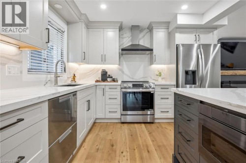 Light-toned wood-finish flooring, white cabinetry with matte black hardware, stainless steel appliances, white countertops, and a white backsplash with veining - 1261 Stephenson Drive, Burlington, ON 