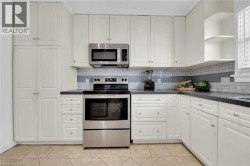 Kitchen with stainless steel appliances, dark countertops, tasteful backsplash, light tile patterned floors, and white cabinets - 