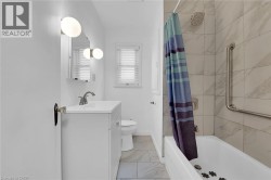 Full bath featuring vanity, marble look tile flooring, shower / bath combo, toilet, and baseboards - 