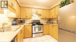 Kitchen with under cabinet range hood, stainless steel appliances, a sink, light countertops, and decorative backsplash - 