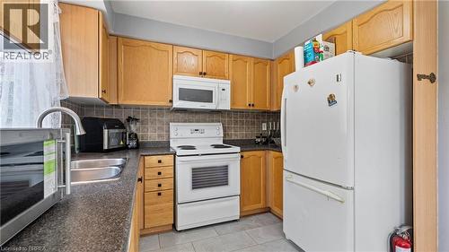 Kitchen featuring wood-finish cabinetry, a double basin stainless steel sink, tile backsplash, and light-toned tile flooring - 124 Osborn Avenue, Brantford, ON 