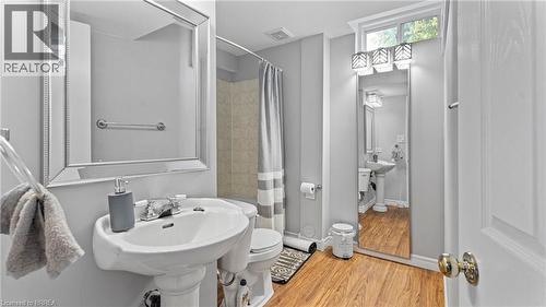 Pedestal sink with chrome faucet, large framed mirror, wood-finish flooring, and a shower with tiled walls - 124 Osborn Avenue, Brantford, ON 