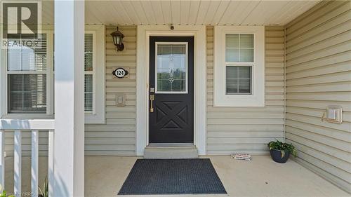 Covered front porch with a paneled black entry door featuring a decorative glass insert, complemented by an exterior wall sconce - 124 Osborn Avenue, Brantford, ON 