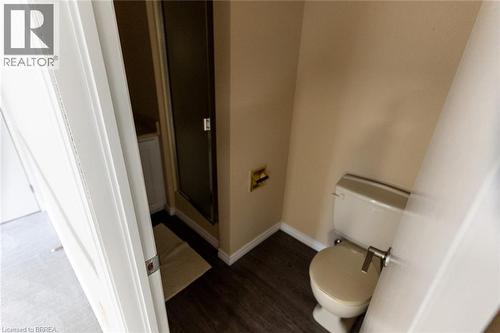 Bathroom featuring wood-finish flooring, a white toilet with a brushed metal flush lever, and a shower enclosure with a dark-framed glass door - 30 Proctor Avenue, Brantford, ON 